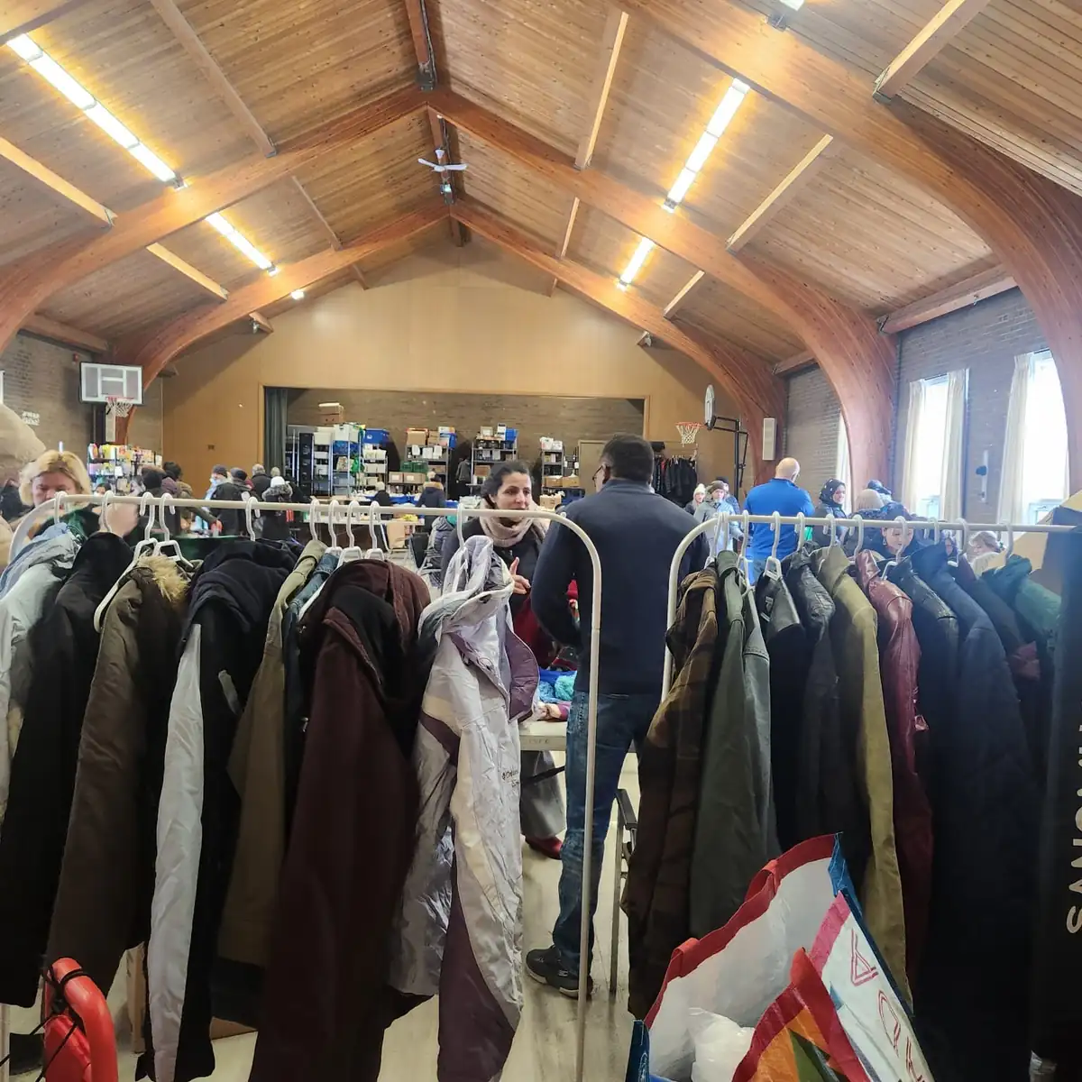 A community member selecting coats from garment racks at a From You To Them clothing distribution